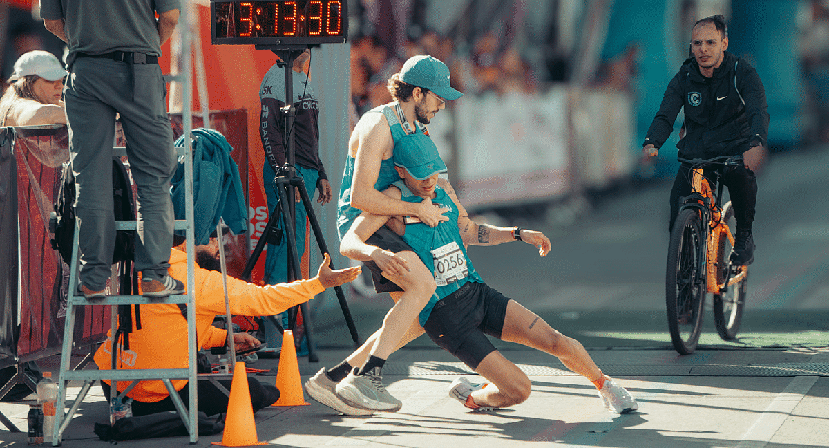 Un coureur soutient un autre participant épuisé sur la ligne d'arrivée.